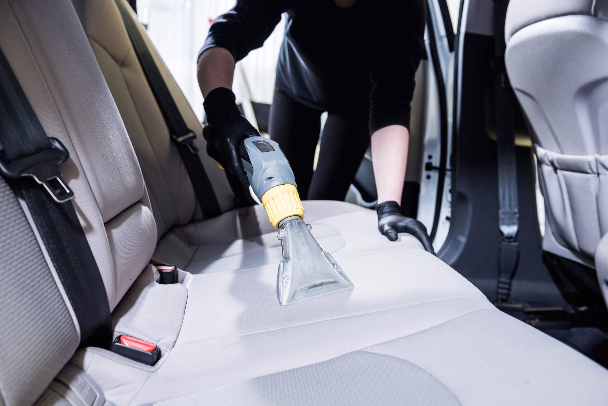 Worker cleans car interior with vacuum cleaner.